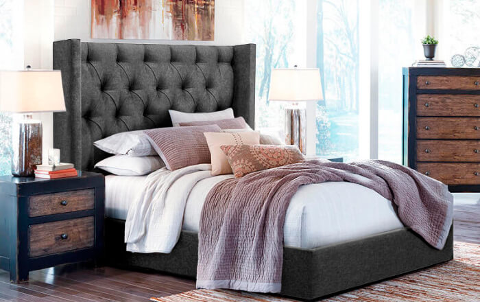 Bedroom with grey bed and headboard with white and light pink bedding complemented by black metal and wooden dresser and pedestal